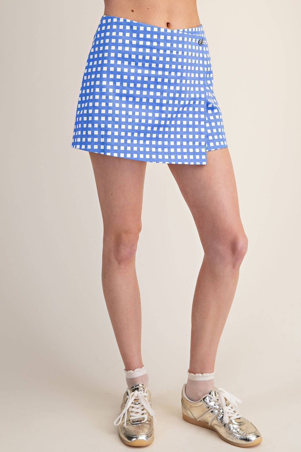 Person wearing a blue and white checkered skirt with silver shoes on a plain background