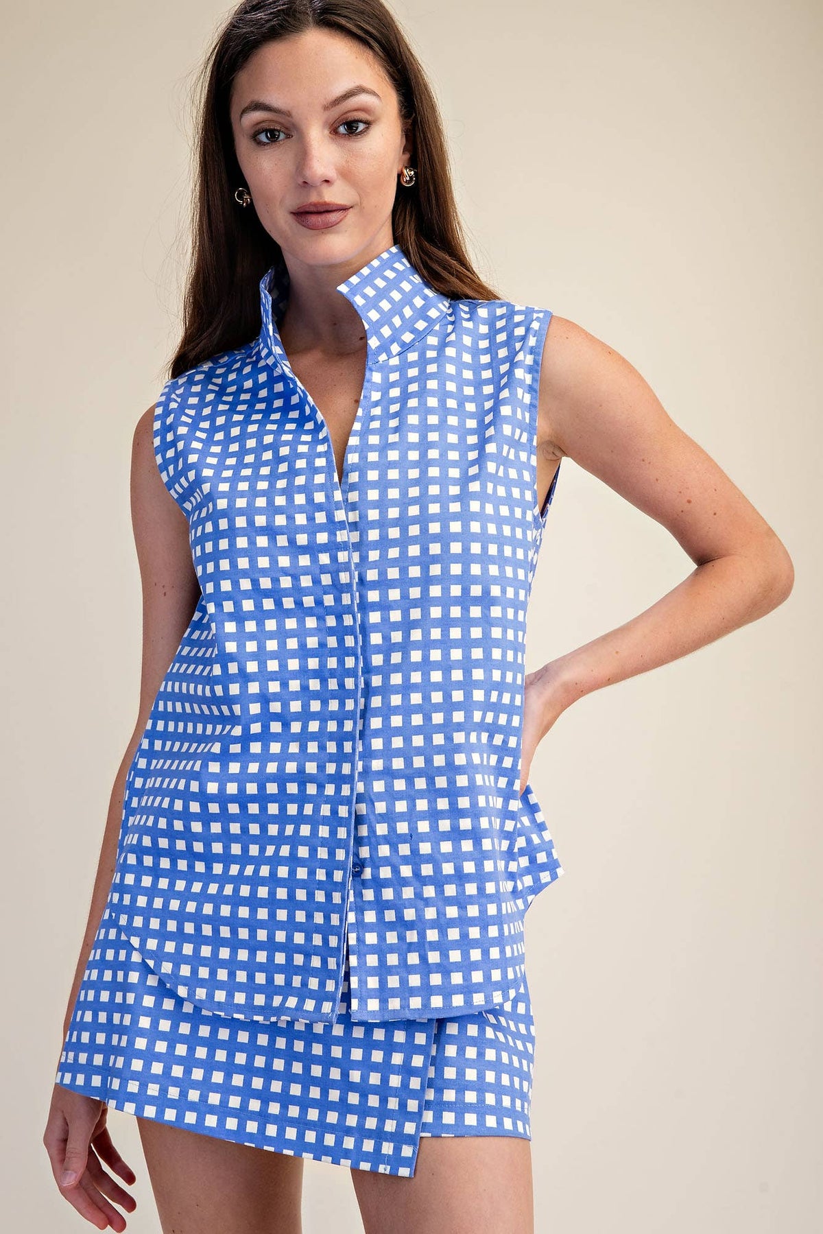 Woman wearing a blue and white checkered sleeveless top and shorts on a beige background