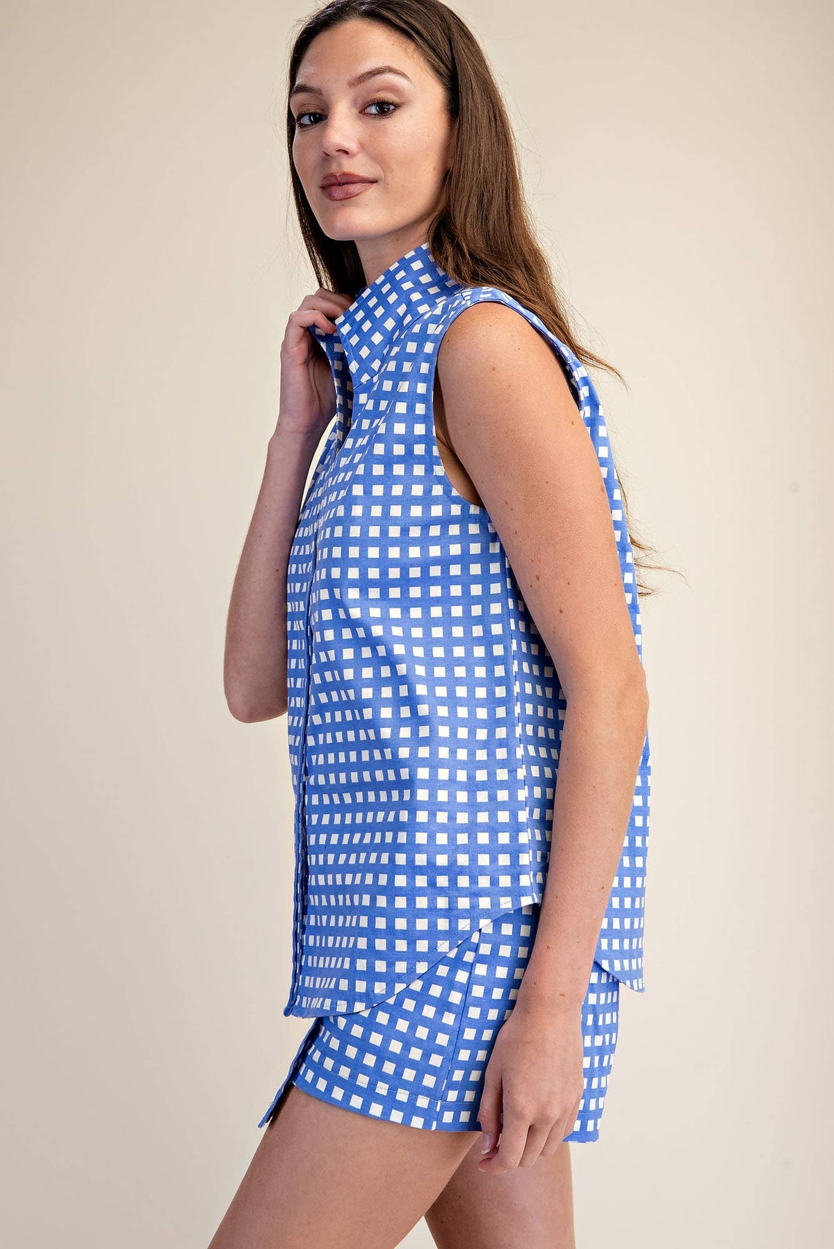 A woman modeling a sleeveless high-neck blue and white gingham mini dress against a plain beige studio background.