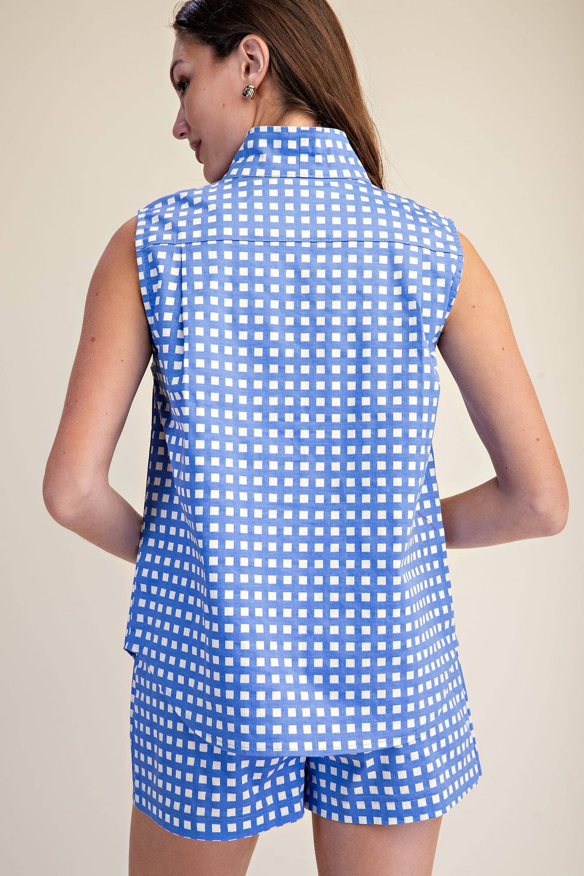 Woman wearing a blue and white checkered sleeveless top and shorts on a beige background