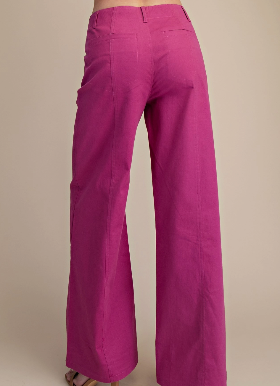 A close-up back view of a person wearing bright magenta wide-leg trousers against a plain beige studio background.