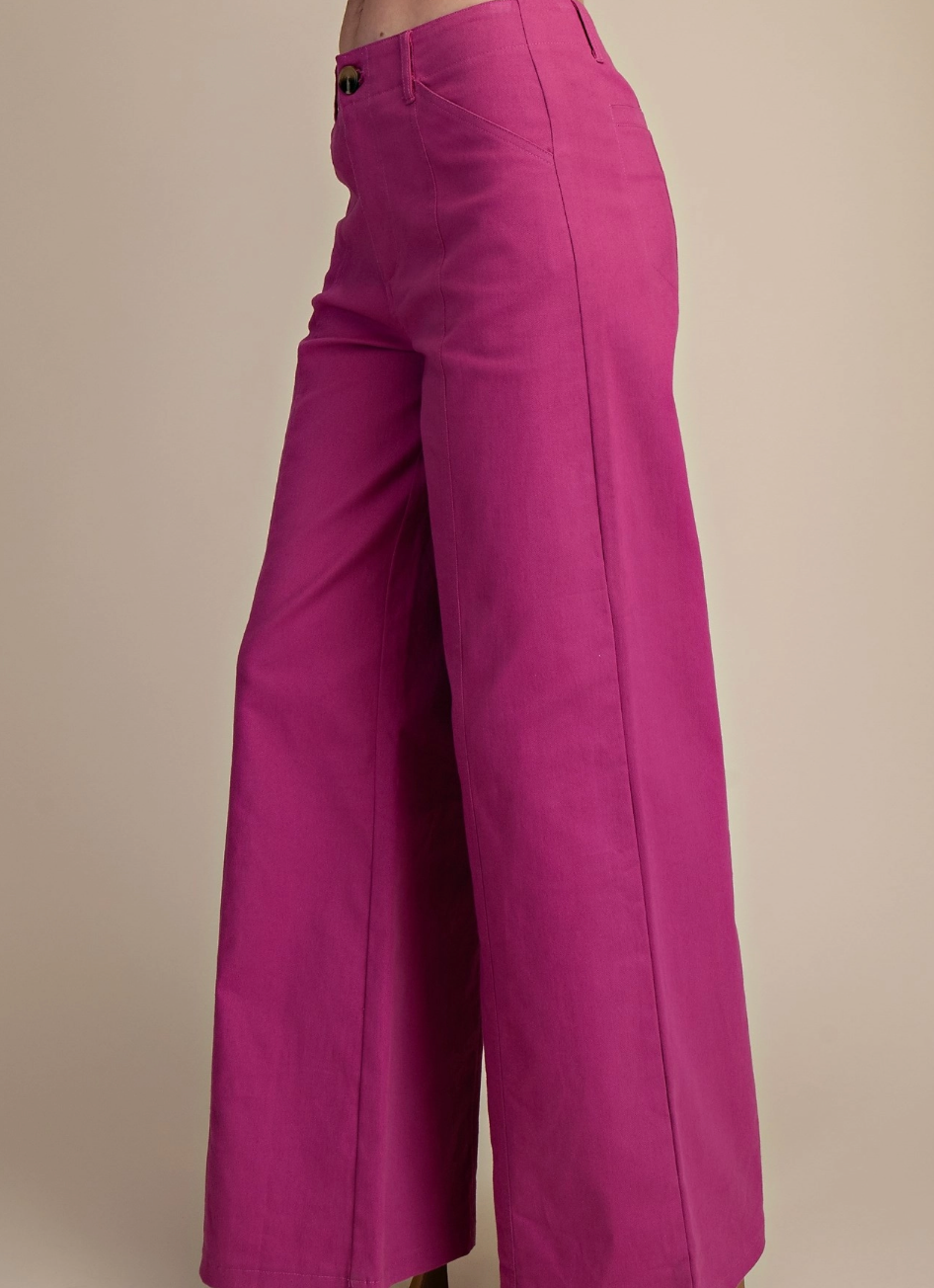 A close-up side view of a model wearing bright magenta wide-leg cropped pants against a solid beige background.