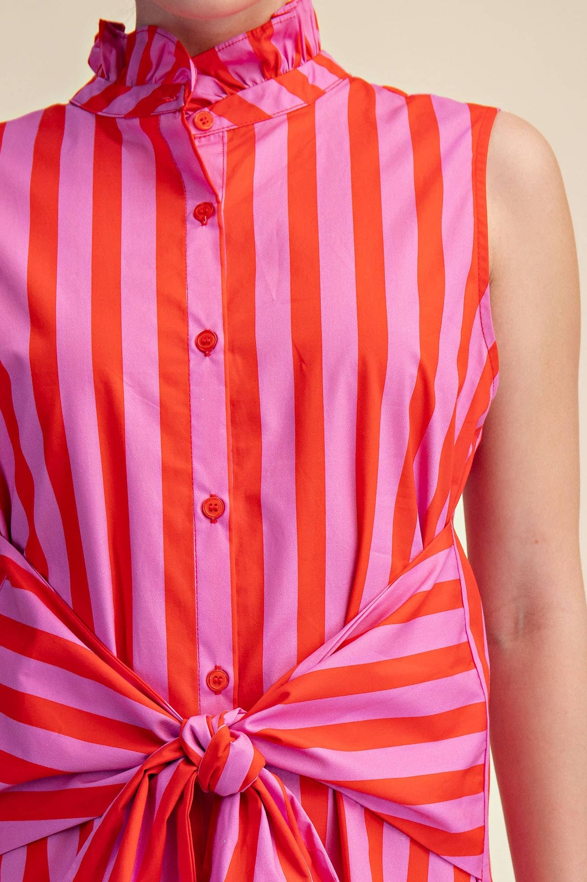 Red and pink striped sleeveless top with a knot detail on a beige background