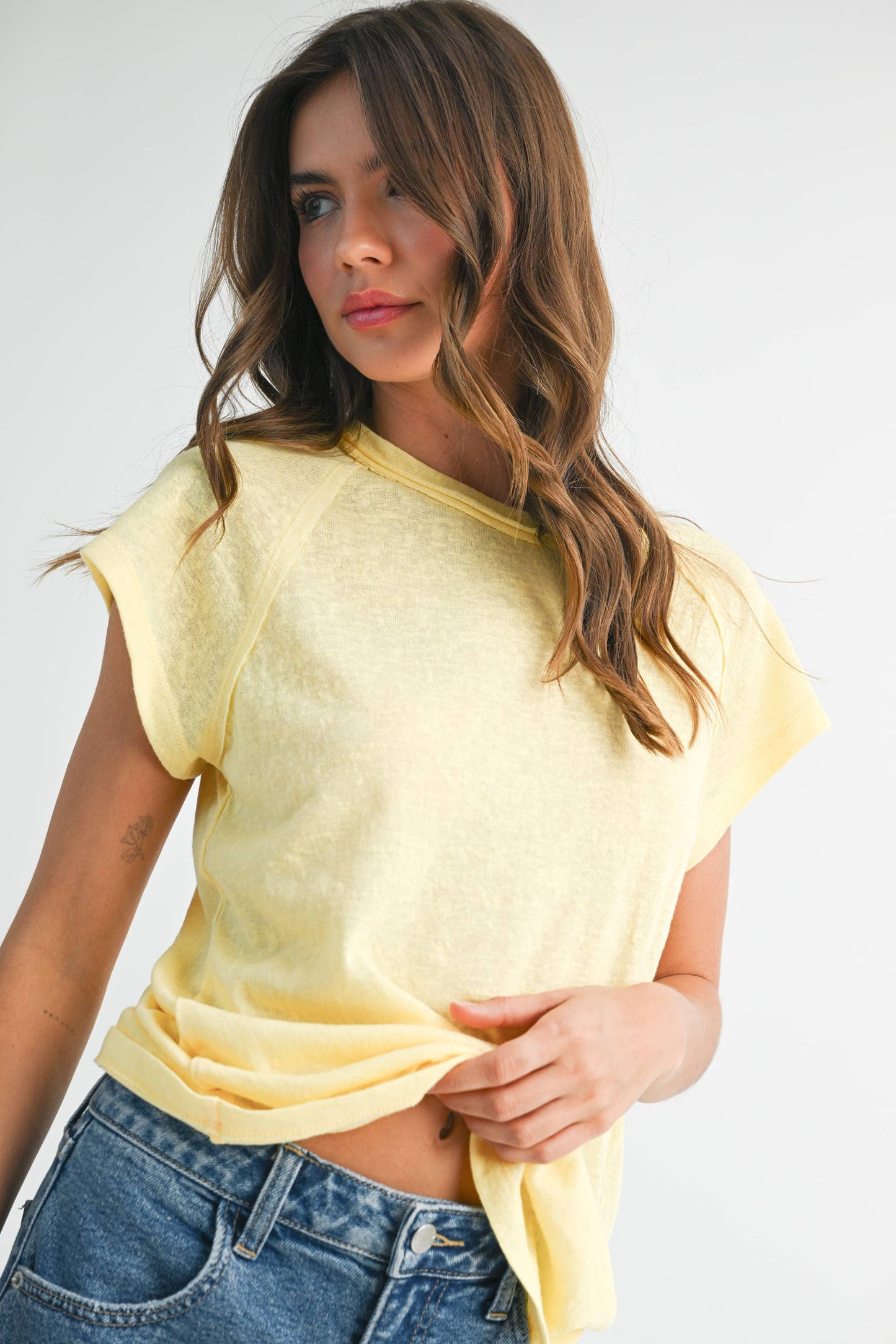 Woman wearing a yellow crop top and blue jeans against a white background