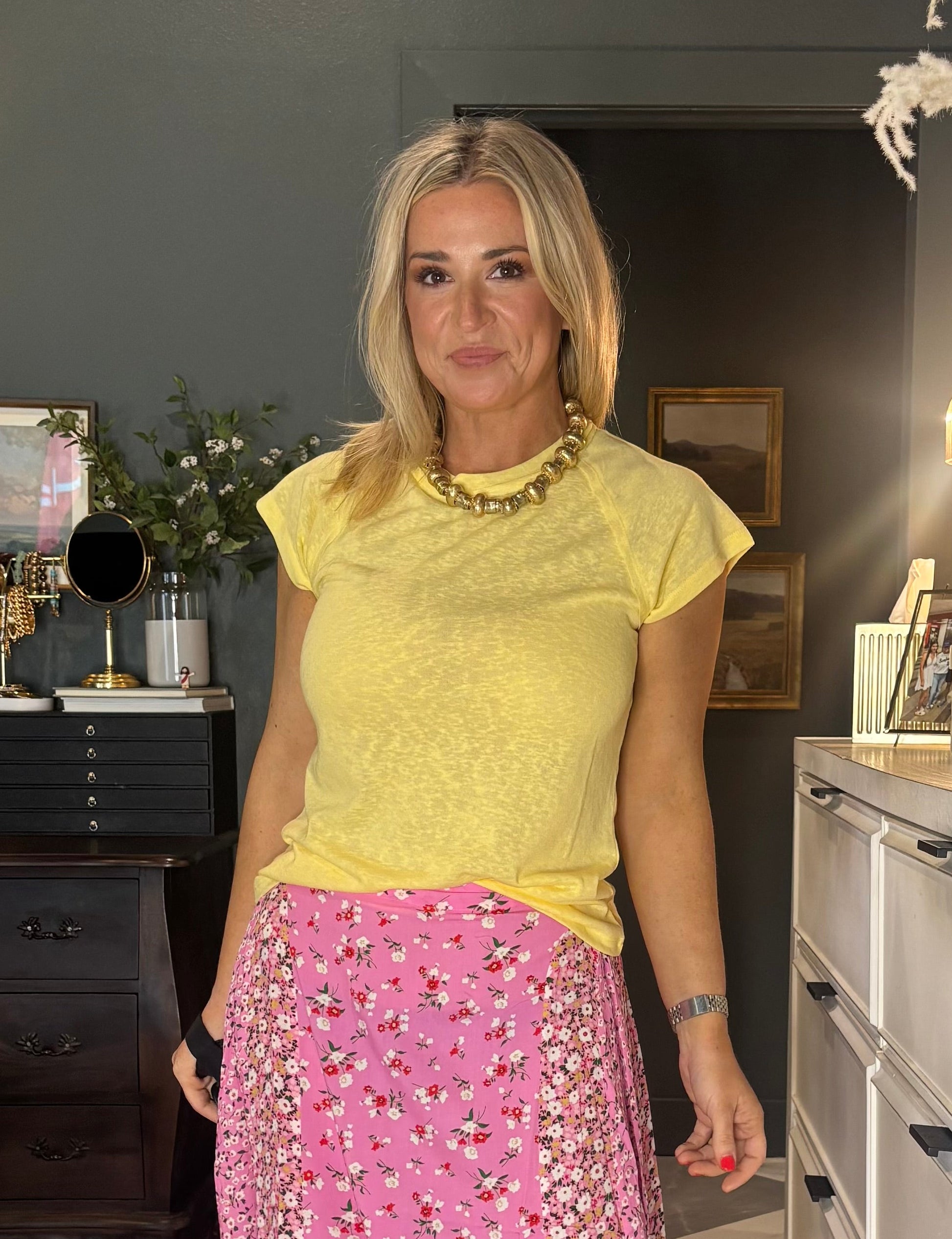 Woman in a yellow top and pink beaded skirt standing in a room with furniture and decor.