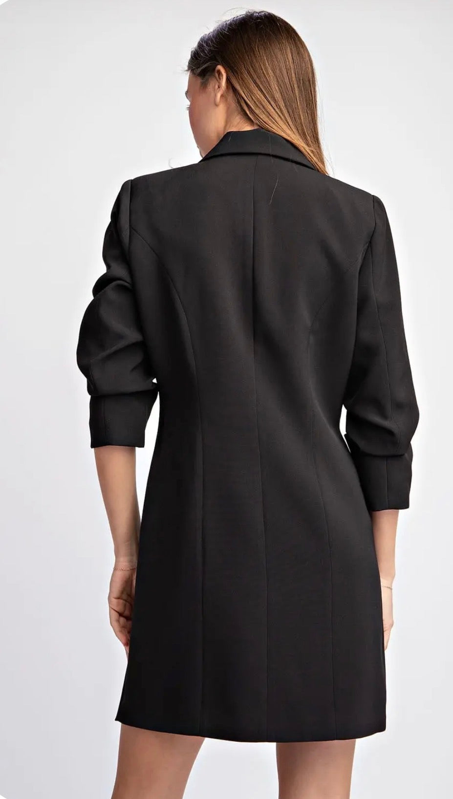 A woman shown from the back wearing a black blazer-style dress with three-quarter sleeves and a structured silhouette, photographed against a light gray studio background.