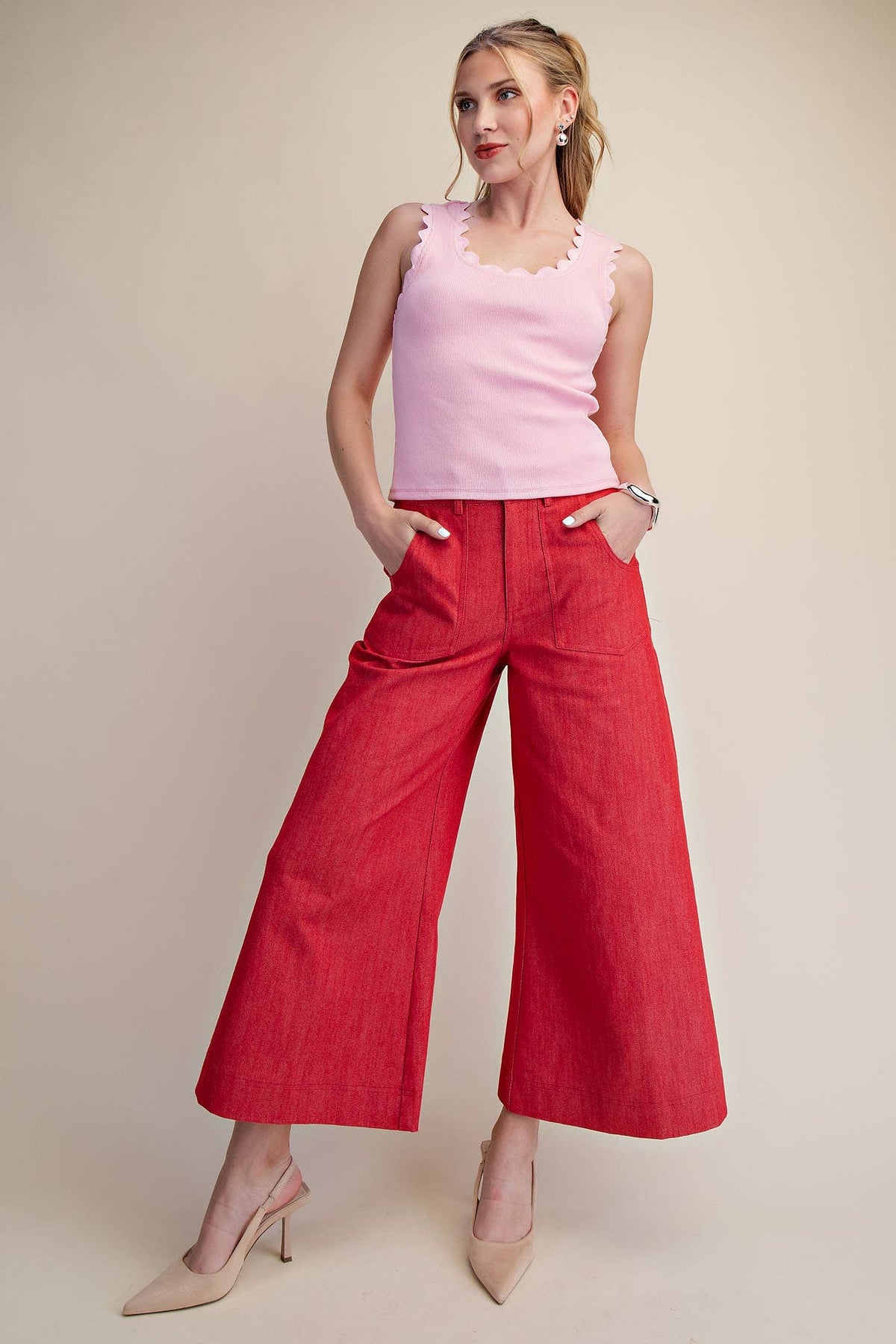 Woman wearing a pink sleeveless top and red wide-leg pants on a beige background