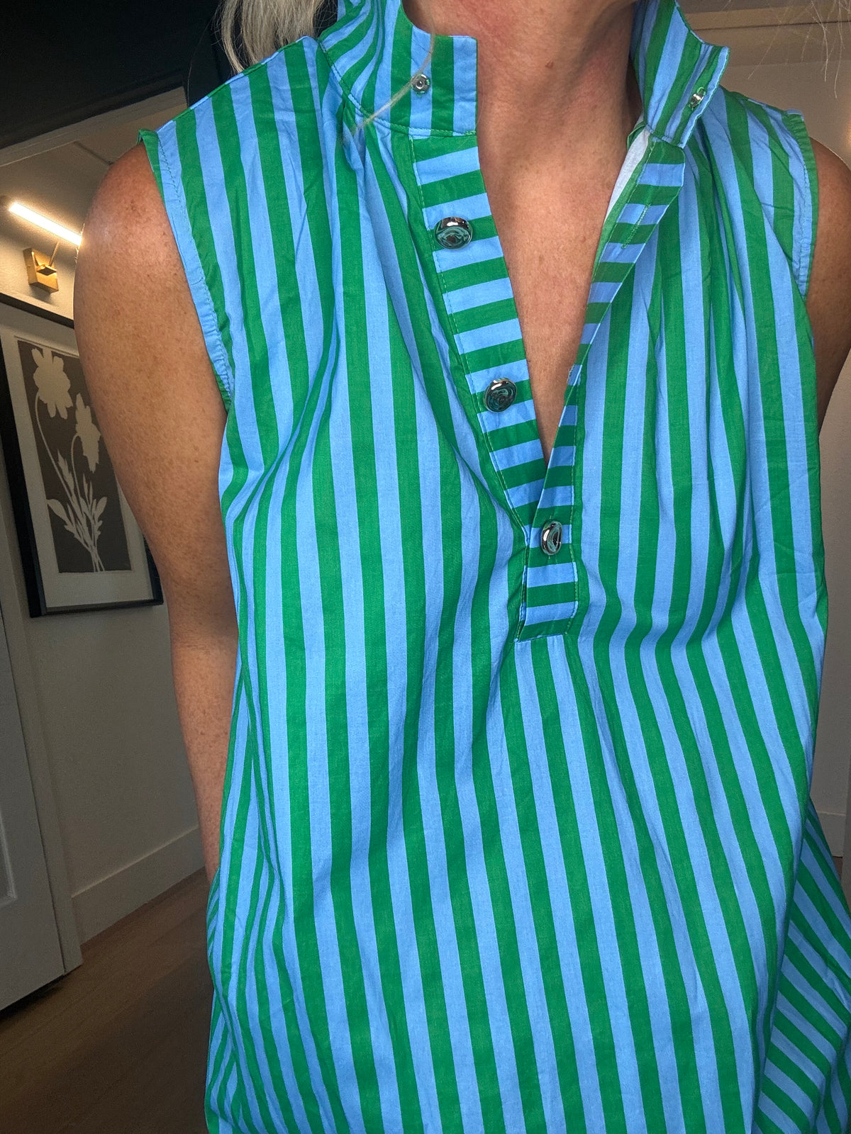 A close-up of a person wearing a sleeveless collared midi dress with vertical green and light blue stripes and a partial button placket.