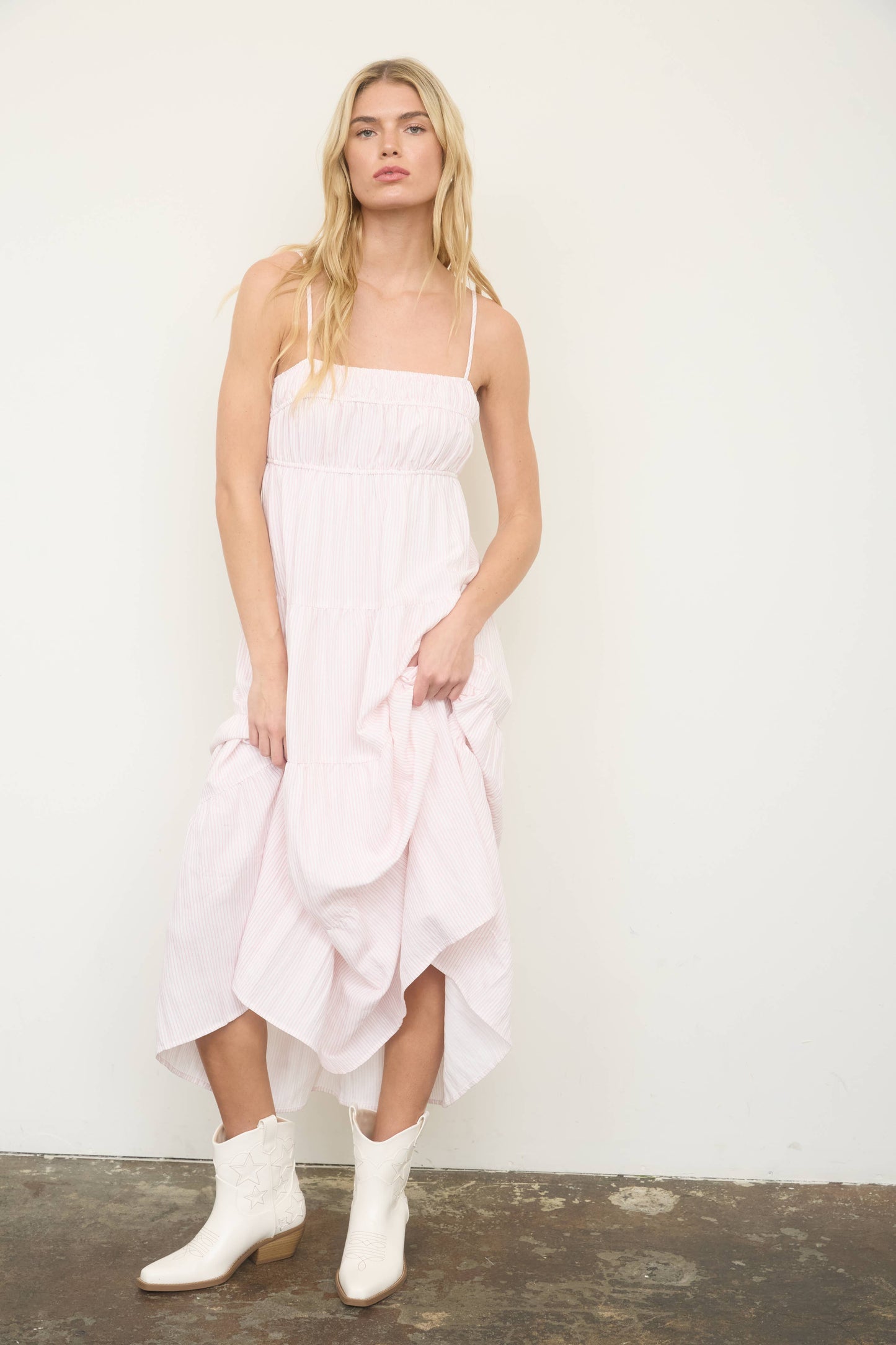 Woman wearing a white dress with ruffled layers and white boots against a plain background