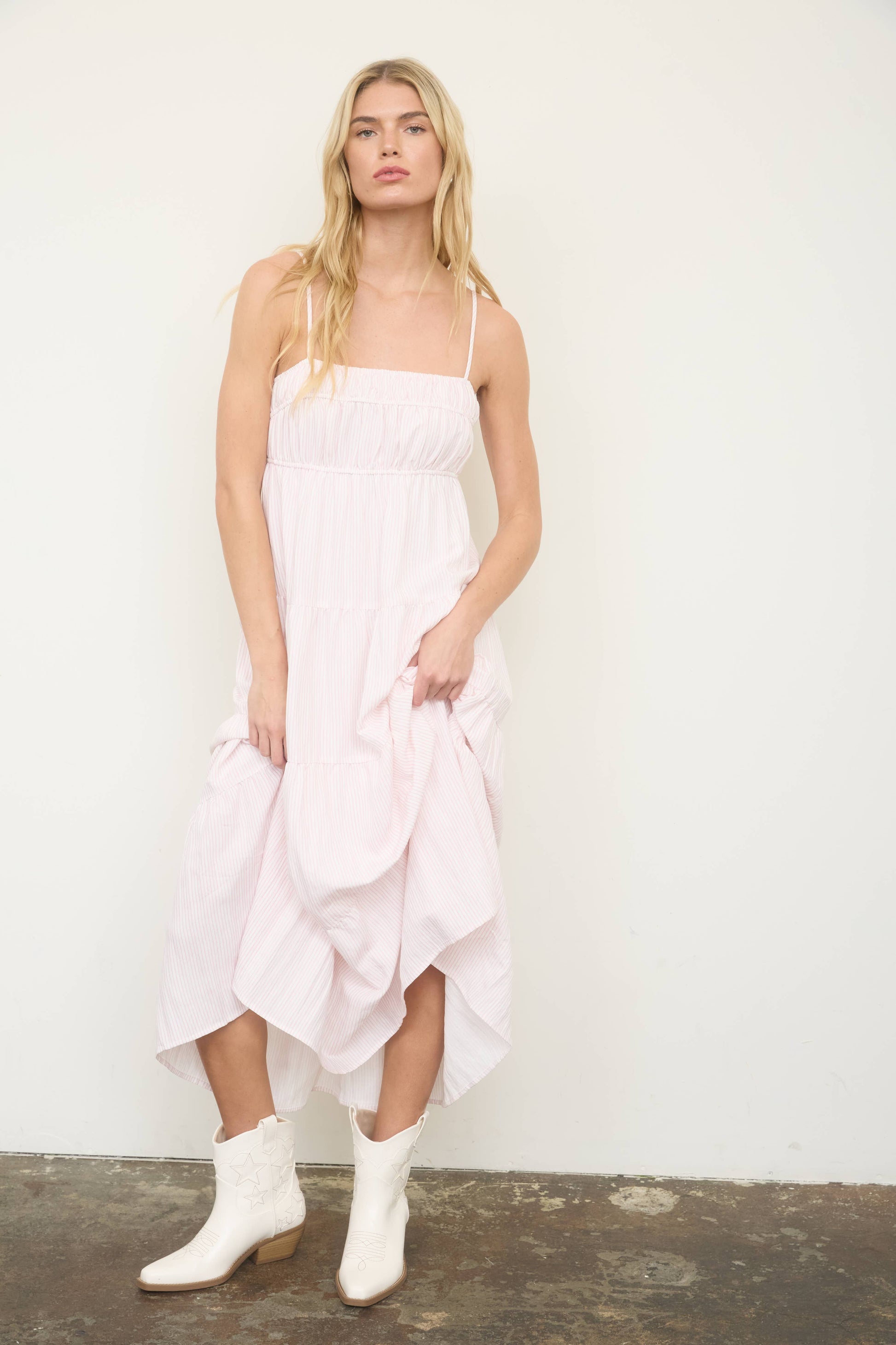 Woman wearing a white dress with ruffled layers and white boots against a plain background