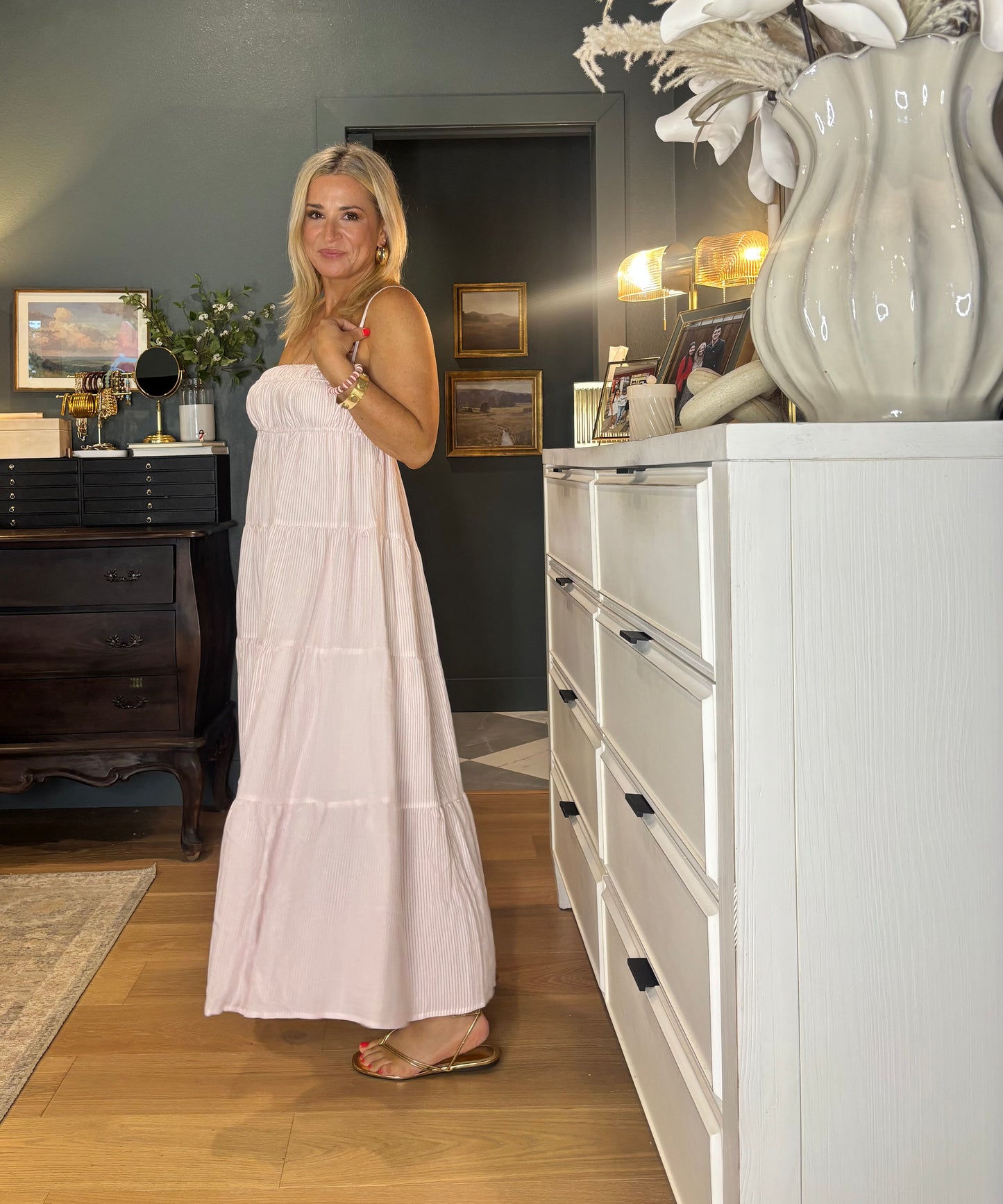 Woman in a white dress standing in a room with a white dresser and decorative items.