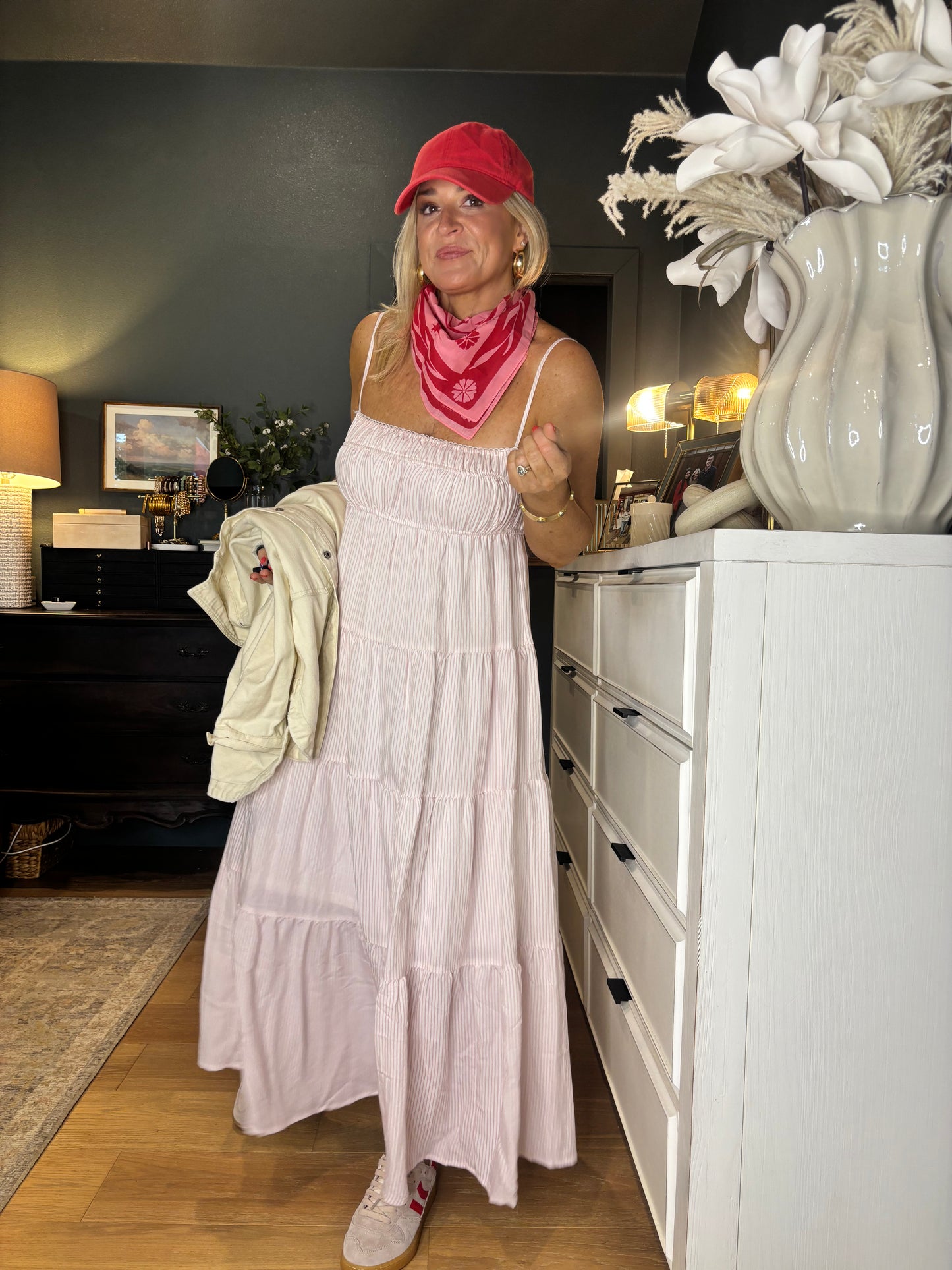 Person wearing a white dress and red hat in a room with a decorative plant and lamp.