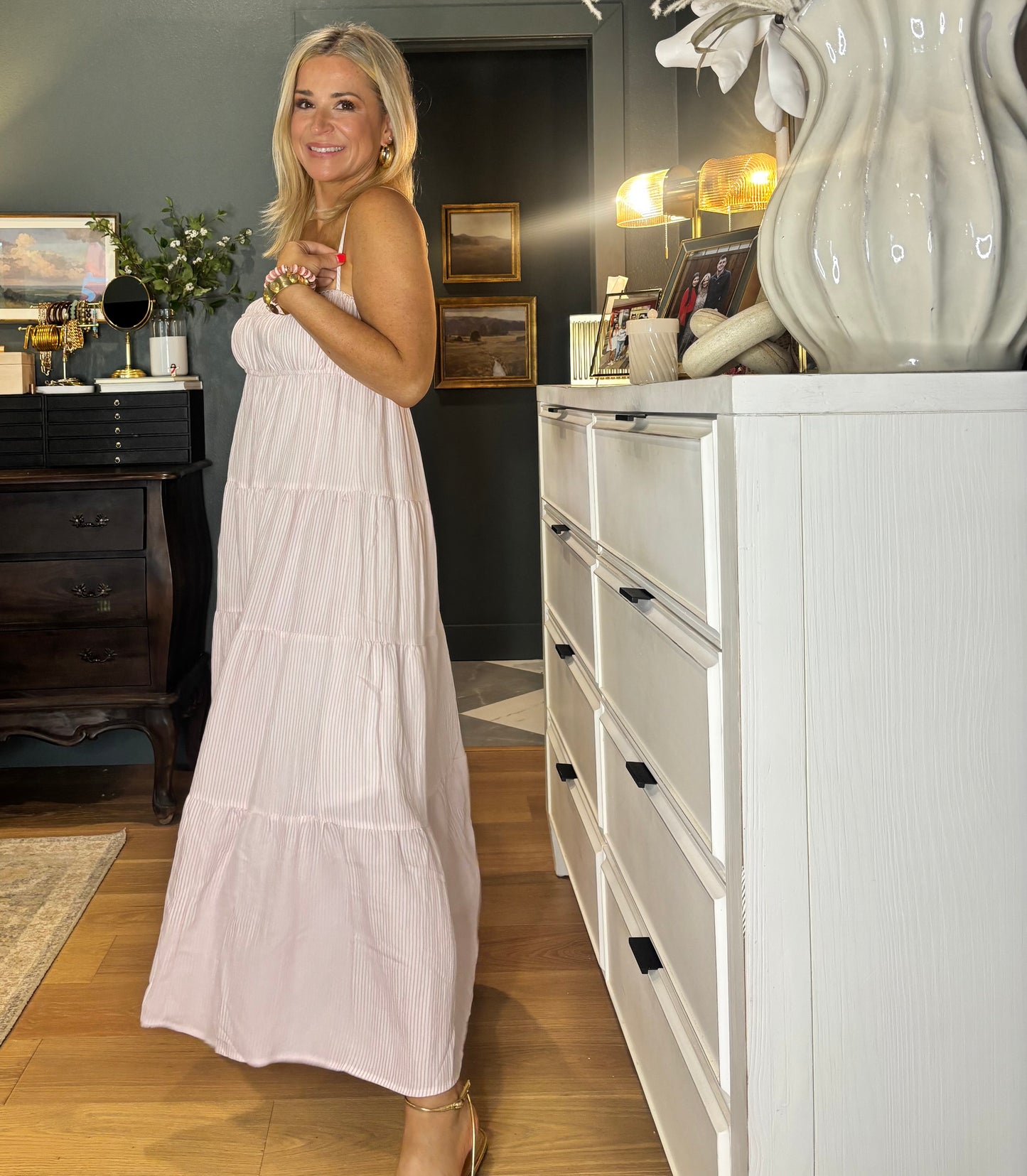 Woman in a white dress standing in a room with a white dresser and decorative items.