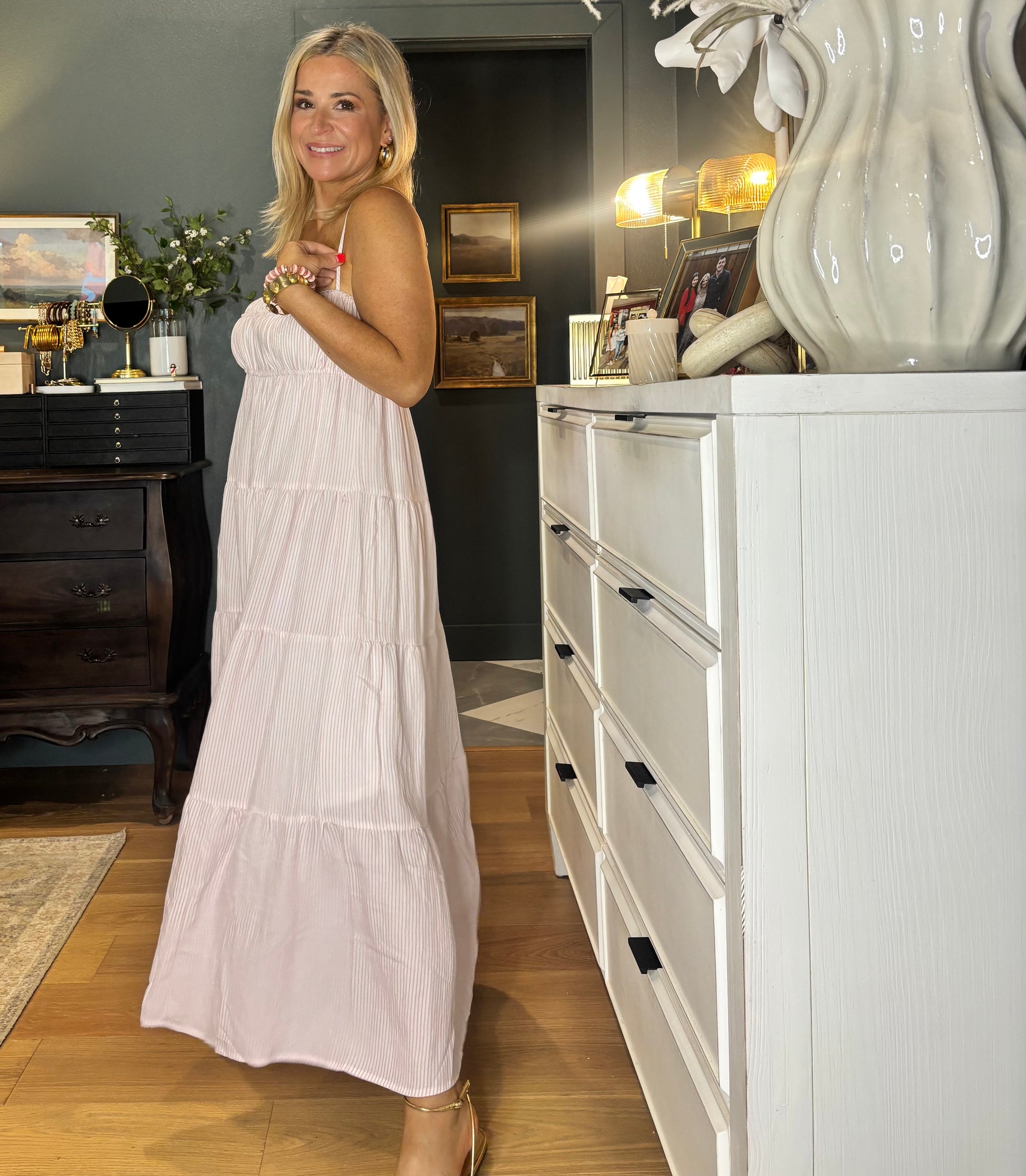 Woman in a white dress standing in a room with a white dresser and decorative items.