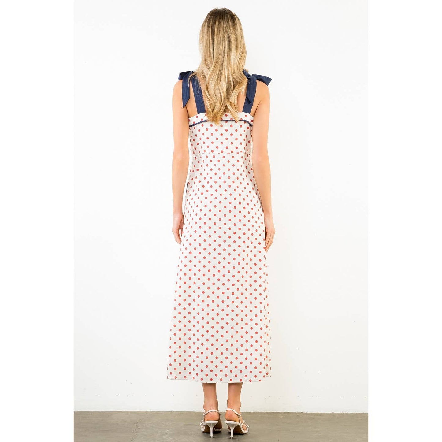 Woman wearing a polka dot dress with blue straps on a white background