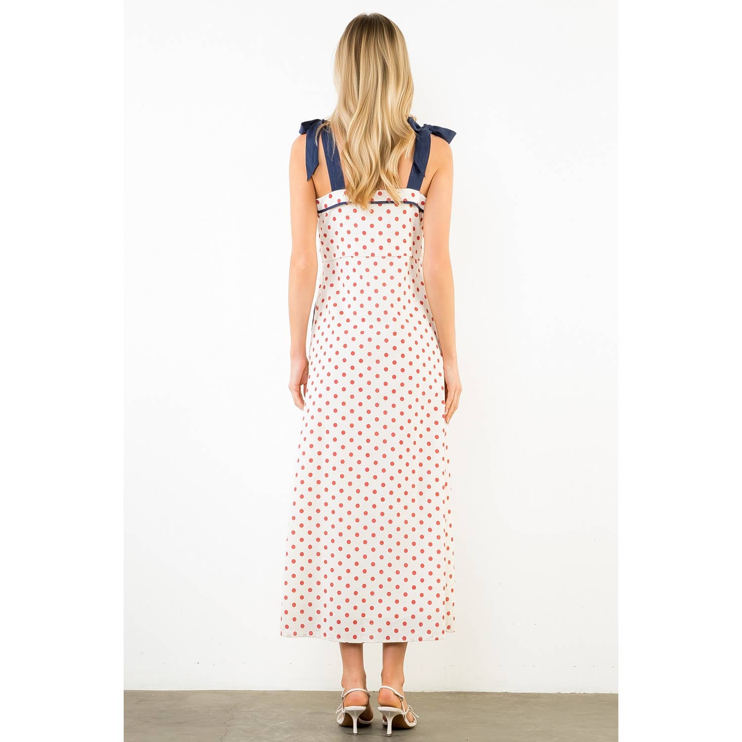 Woman wearing a polka dot dress with blue straps on a white background
