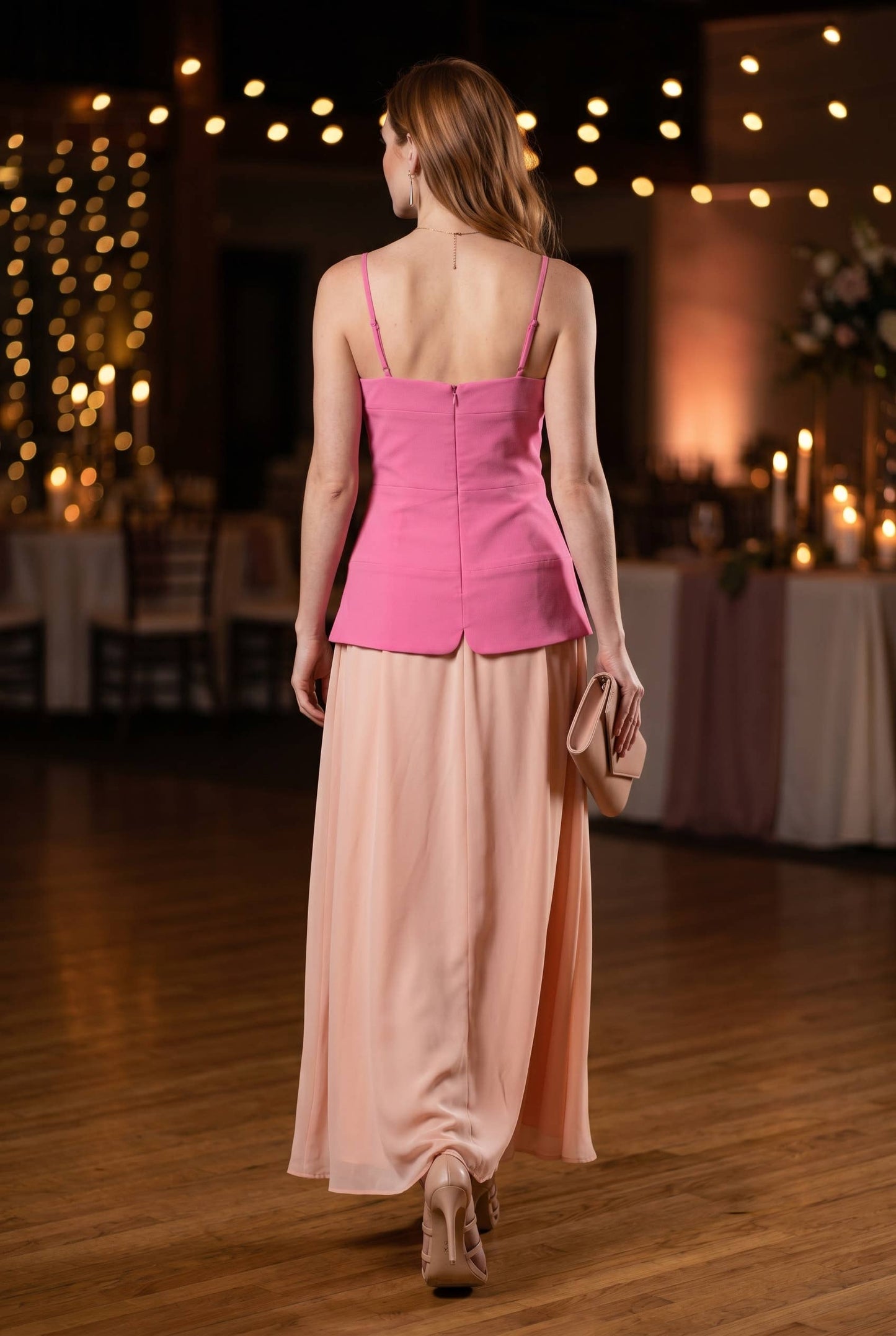 Woman in a pink top and beige skirt walking in an elegant indoor setting with string lights.