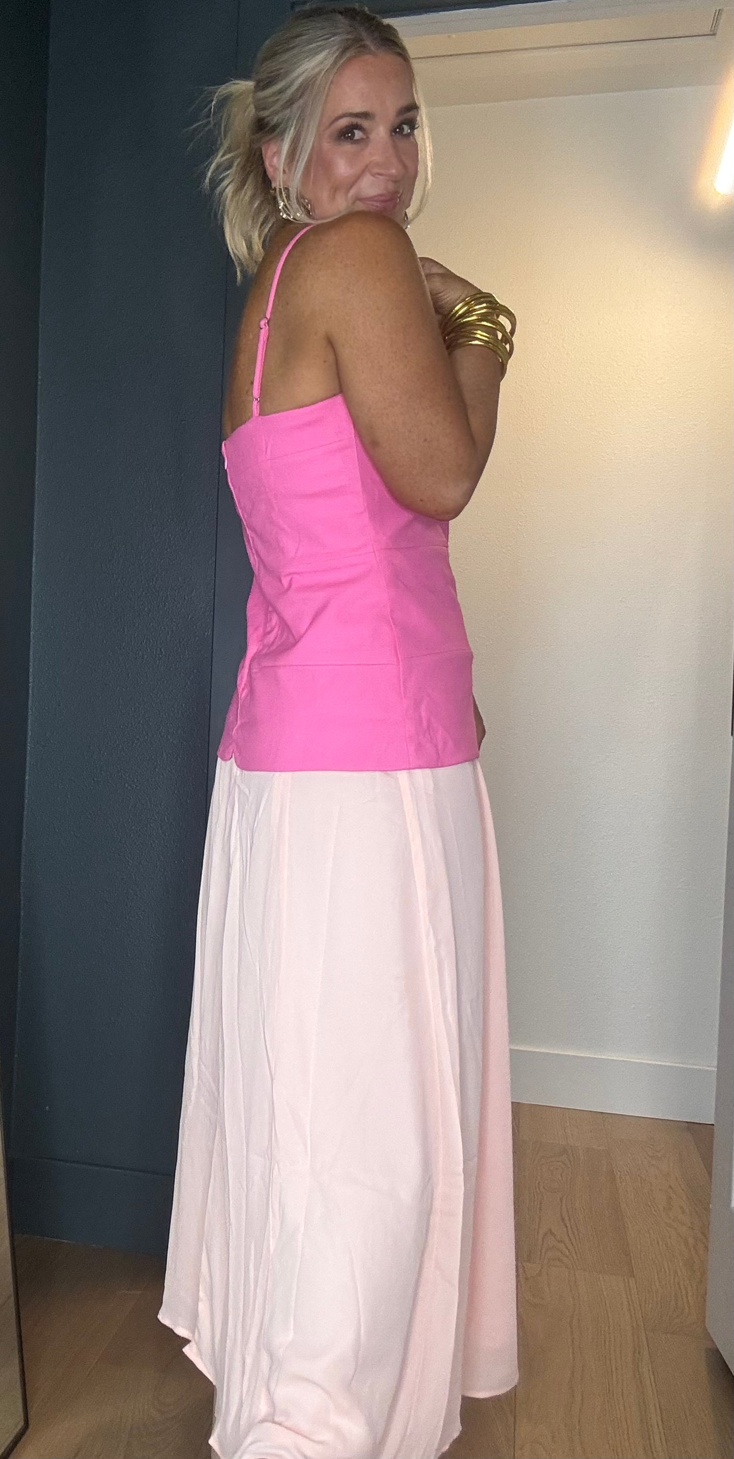 A woman wearing a bright pink sleeveless midi dress with thin straps and three large mesh star-shaped cutouts down the front, paired with a long light peach skirt.
